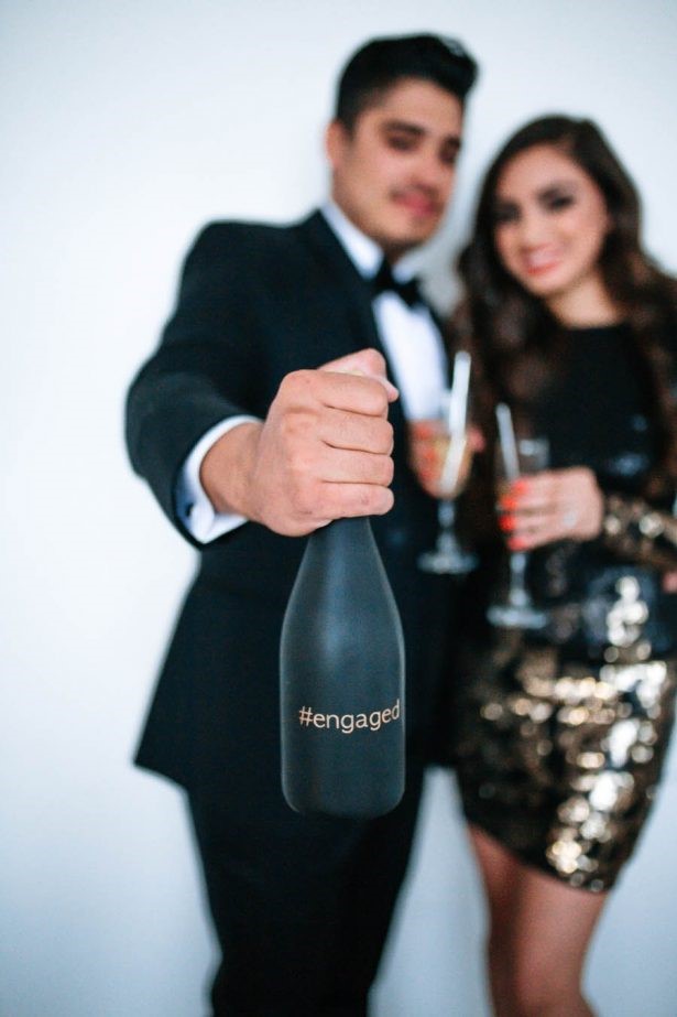 A selfie picture of a newly engaged couple with a bottle of champagne